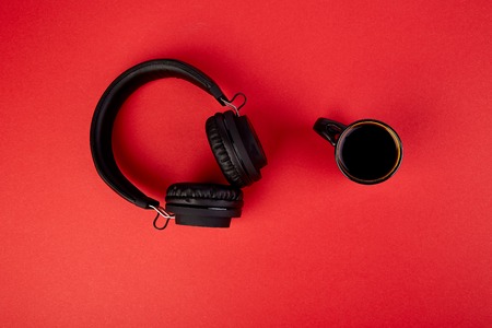 Black Headphones and cup of coffee on red background. Flat lay. Top view. Copy space.