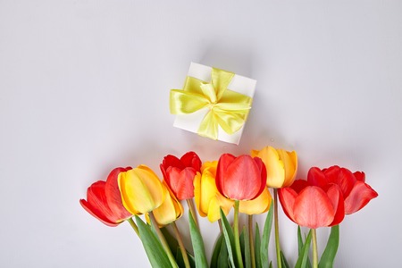 White gift box with yellow ribbon near bouquet yellow red tulip on white background. Flat lay. Mother or Woman  Day. Greeting Card. Copy space. Spring. の写真素材