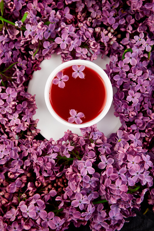 Cup of tea and branches of spring flowers bouquet blooming lilac on black table.
Creative design of flowers.Flat lay. Place for text.の写真素材