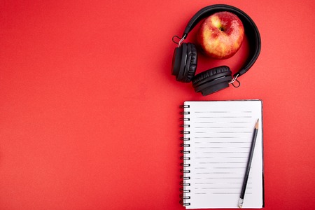 Black Headphones and apple with notebook, note on red background. Flat lay. Top view. Copy space.の写真素材