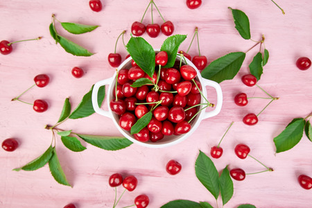 Red cherry in white bowl on pink background. Summer or spring concept. Harvest. 
Some cherries near the bowl. Flat lay. Top view.の写真素材