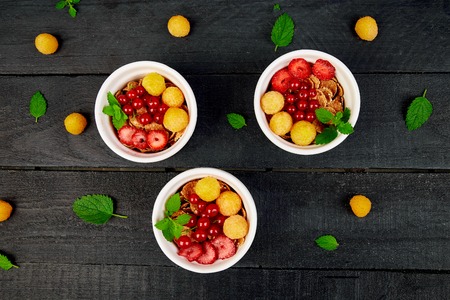 Healthy breakfast on white bowls. Fresh granola, muesli or cereal with berries - yellow raspberry, currents and strawberry on black background. Diet food. Clear food. Top view. Copy space. Flat lay.の写真素材