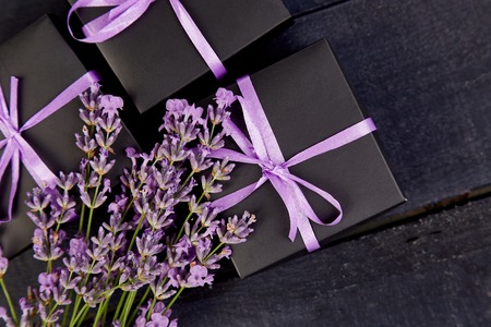 Black Gift box with violet ribbon and bouquet of flower lavender on black background. Celebration, birthday. Decoration present. Flat lay. Copy space.の写真素材