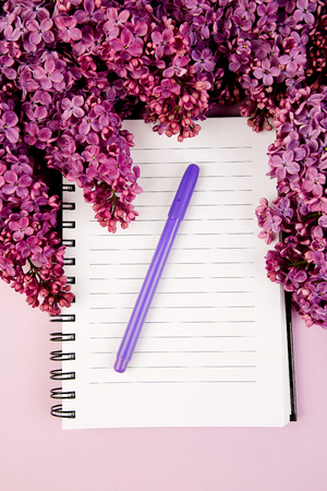 Branches of spring flowers bouquet blooming lilac on purple table. Woman diary notebook. Creative design of flowers. Flat lay. Place for text.の写真素材