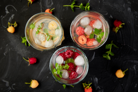 Detox infused flavored water with three color raspberry - red, orange, yellow on black background.. Refreshing summer homemade cocktailの写真素材