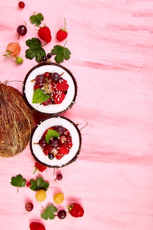 Fruit salad agrus, gooseberry, rasbberry in coconut shell bowl on a pink table background, healthy and delicious, breakfast or dessert. Diet food. Vegan concept. Flat lay. Top view. Copy cpace.の写真素材