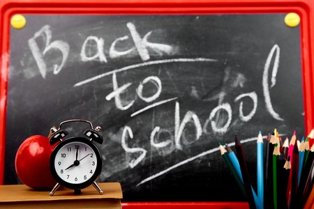 Back to school lettering on  blackboard with piece of chalk with books, pencils, red apple near chalkboard background.
Still life with school books and alarm clock against blackboard.の写真素材