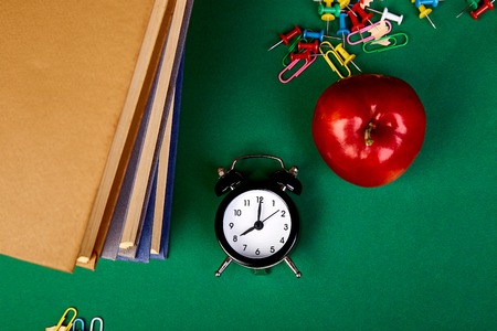 Back to school supplies. Books and red apple on green background. Still life with alarm clock. Flat lay. Top view. Copy space.の写真素材