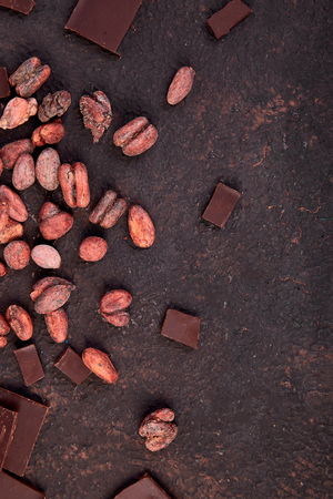 Cocoa beans background on brown table. Dark chocolate pieces and crushed cocoa powder carob. Top view. Copy space.の写真素材