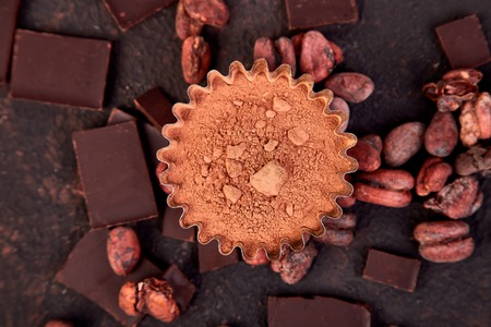 Cocoa beans background on brown table. Dark chocolate pieces and crushed cocoa powder carob. Top...