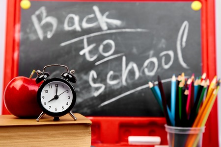 Back to school lettering on  blackboard with piece of chalk with books, pencils, red apple near...