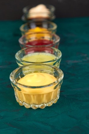Set of different sauces. Sauces ketchup, mustard, mayonnaise, wasabi, soy sauce in little bowls on green backgroundの写真素材