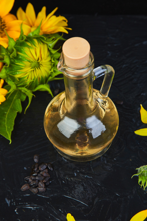 Sunflower oil in glass jar, sunflower seeds and fresh flowers on black table background. Bio and organic product concept. Space for text.の写真素材