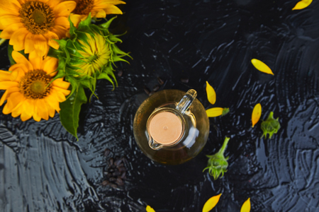 Sunflower oil in glass jar, sunflower seeds and fresh flowers on black table background. Bio and organic product concept. Space for text.の写真素材