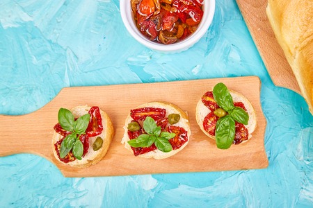 Bruschetta or crostini with sun dried tomatoes and capers on a wooden kitchen board with blue background. Fresh italian sandwiches.Delicious snack and appetizer. Antipasto. Falt lay. Copy space.  top view.の写真素材