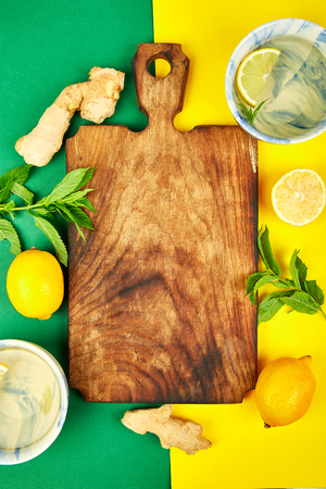 Ingredients for hot tea with ginger, lemon, mint and cups around cutting board on green yellow background. Flat lay. Top view. Copy space.の写真素材