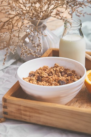 Good morning. Breakfast on white bed sheets. Muesli or granola, milk, orange  on wooden tray from above. Top view.  Flat lay. Copy space. Hotel Room Early Morning.の写真素材