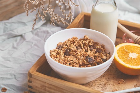 Good morning. Breakfast on white bed sheets. Muesli or granola, milk, orange  on wooden tray from above. Top view.  Flat lay. Copy space. Hotel Room Early Morning.の写真素材