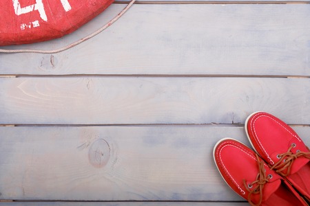Red boat shoes on wooden near lifebuoy and rope. Top view. Copy space. Flat lay