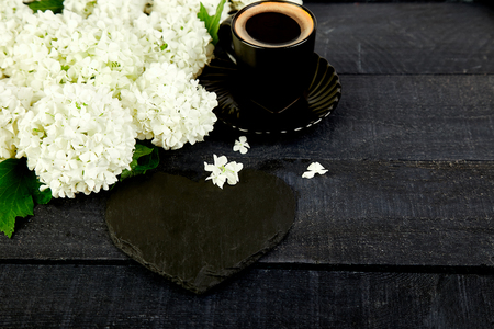 Cup of coffee with bouquet flower hydrangea and slate heart on black woodenの写真素材