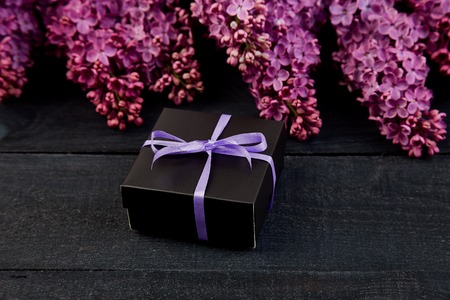 Black small gift boxes wrapped with violet , purple  ribbon decorated with flower natural lilac. Floral decor elements. Copy space. Place for text.の写真素材