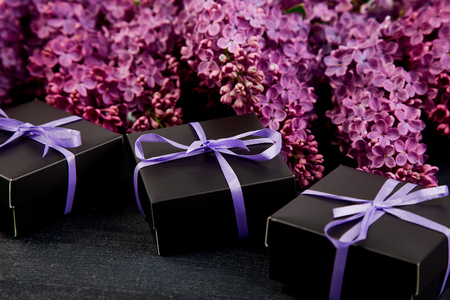 Black small gift boxes wrapped with violet , purple  ribbon decorated with flower natural lilac. Floral decor elements. Copy space. Place for text.の写真素材