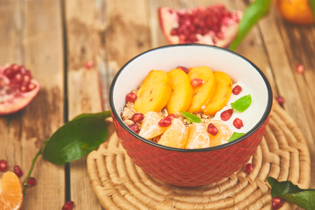 Tropical fruit  smoothies bowl Breakfast homemade granola yogurt pomegranate, tangerine, persimmon on wooden rustic background. healthy organic layered dessert. Diet, vegan food. Top Viewの写真素材