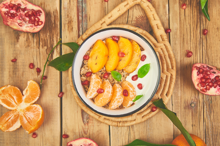 Tropical fruit  smoothies bowl Breakfast homemade granola yogurt pomegranate, tangerine, persimmon on wooden rustic background. healthy organic layered dessert. Diet, vegan food. Top Viewの写真素材