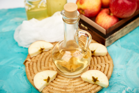 Glass Bottle of apple organic vinegar on blue background. Apple cider vinegar. 
Healthy organic drink food. Bottle of fresh cider near autumn red apples. Space for textの写真素材