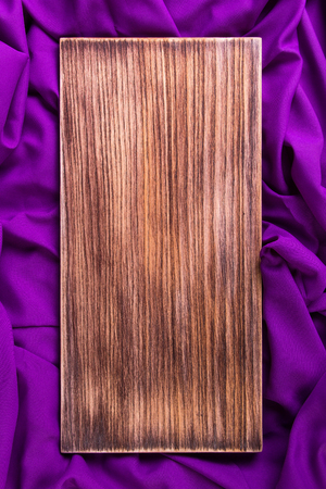 Wooden cutting board on purple, violet napkin cloth background. Flat lay. Copy space, Top view.の写真素材