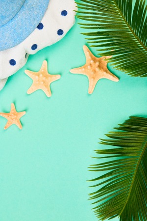 Summer female fashion outfit. Sunhat, polka dot towel, and starfish with tropical palm branches on blue background. Beach, vacation, travel concept, Minimalism.  Flat lay, top view. Copy space.の写真素材