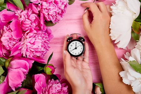 Florist at work, Hands of woman hold alarm clock. Deadline. florist beautiful bouquet of peonies. Flat lay. Top view. Time to work or rest.の写真素材