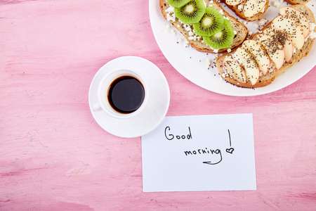 Coffee mug and healthy toasts and notes good morning on pink table. beautiful breakfast, greeting card, top view, flat lay. Copy space.の写真素材