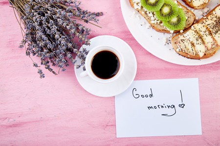 Coffee mug and healthy toasts breakfast  with bouquet of flowers lavender and notes good morning on pink table.の写真素材