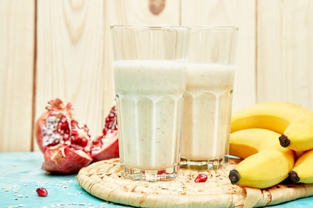 Smoothie with oat or oatmeal, banana and pomegranate on blue background. Healthy drink breakfast. Diet milkshake with protein.の写真素材