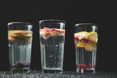 Variety of  Detox infused water with  kiwi, apple, lavender, ginger, lemon, mint on black background. Refreshing summer homemade cocktail. Diet. Healthy drink. Copy space.の写真素材