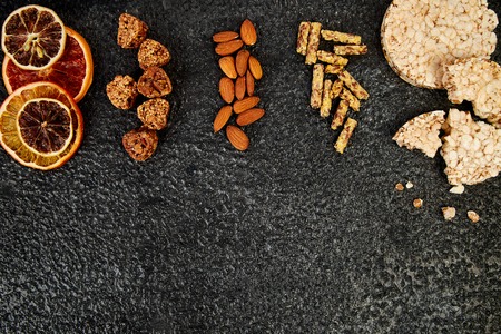 Healthy snacks -  variety oat granola bar,  rice crips, almond,  kiwi, dried orange, on black...