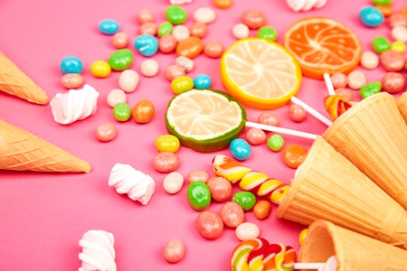 Ice cream waffles cones with colorful candy, sweets jelly, lollipop on stick, scattering of multicolored sweets on pink background. Flat lay, Top view. Copy space.の写真素材