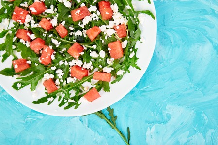 Fresh summer watermelon salad with feta cheese and arugula on blue table background. Vegan food. Diet, Vegetarian. Top view. Flat lay. Copy spaceの写真素材