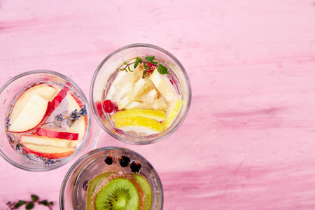 Variety of  Detox infused water with  kiwi, apple, lavender, ginger, lemon, mint on pink background. Refreshing summer homemade cocktail. Diet. Healthy drink.  Top view. Copy spaceの写真素材