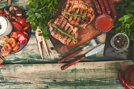 Grilled meat. Steak pork grill on wooden cutting board with a variety of grilled vegetables on  rustic background  Top view. Flat lay. Copy space.の写真素材