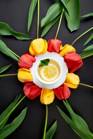 Cup of tea with red and yellow tulip around. Concept about tea drinking.の写真素材
