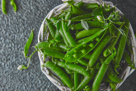 White Basket with fresh green peas on black background. Vegan and vegetarian food concept. Flat lay.の写真素材