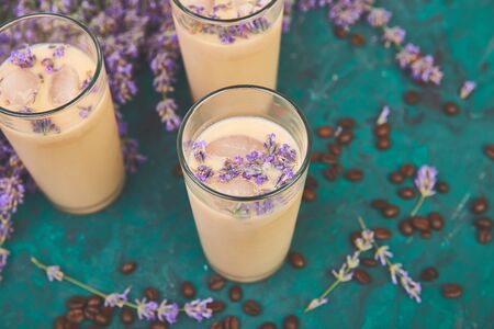 Summer drink iced coffee with lavender in glass and coffee beans on green