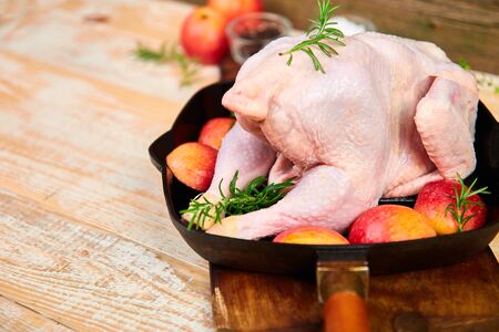 Whole raw chicken in skillet  or iron pan with rosemary leaf, thyme, lemon, red apples . Ready to cook. Cooking background. Copy spaceの写真素材