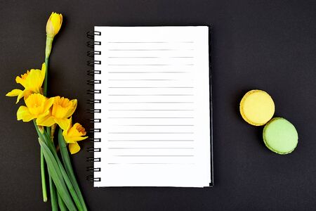 Top view flat lay empty notebook with spring flowers narcissus and macaroons dessert on black background. Text space. To doi list.の写真素材