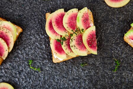 Healthy breakfast toasts from sliced watermelon radish or chinese daikon, chia and cottage cheese on black background. Top view. Flat lay. Copy space.の写真素材