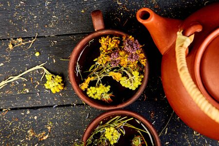Two  Cup of herbal tea - tutsan, sagebrush, oregano, helichrysum, lavender near brown teapot on dark wooden background. Herbal tea. Dry Herbs and flowers, herbal medicine.  Flat lay.の写真素材