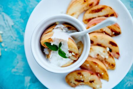 Grilled peach with ice creame on white plate on blue background. Grilled dessert. Barbecue fruit. Copy space. Healthy food. Vegan food.の写真素材
