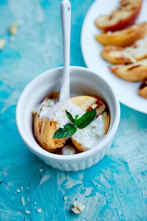 Grilled peach with ice creame on white plate on blue background. Grilled dessert. Barbecue fruit. Copy space. Healthy food. Vegan food.の写真素材